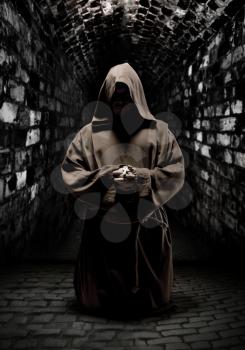 Mystery monk praying on kneels in dark temple corridor