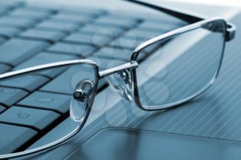 Businessman's glasses on laptop computer. Toned in blue