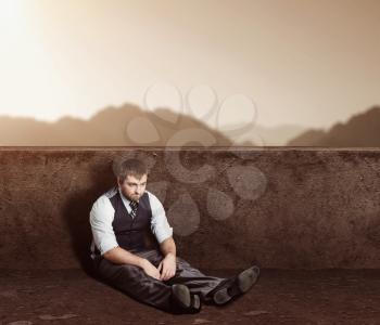 Portrait of depressed man sitting on the floor in desert