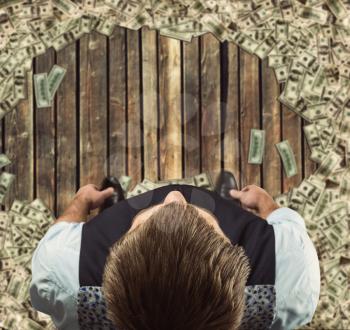 Up view of businessman standing on a wooden floor surrounded with money