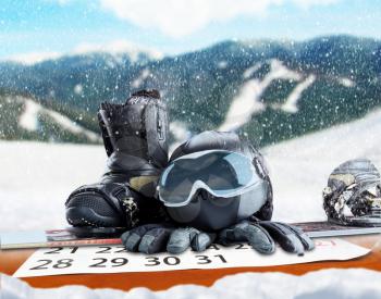 Winter sport glasses, snowboard, helmet, gloves and calendar on winter forest and mountains background