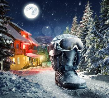 Snowboard boot with helmet and goggles in winter village at night