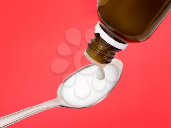 Liquid medicine dropping from a bottle on a spoon