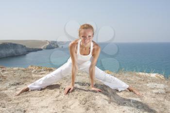 Beautiful woman in white cloth practices Yoga in mountains against the sea