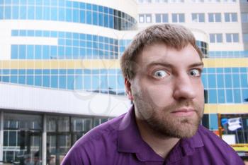 Strange bearded adult man looks at you over building background