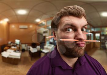 Strange bearded man holds pencil with his nose and lips and one more pencil in his ears