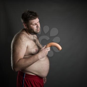 Side view of fat man with a sausage in his hand. Potency problem