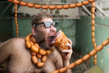 Hungry man with sausages round his neck eats a big wurst in the room with sausages