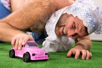 Shirtless man weared as baby playing with violet car