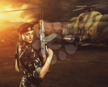 Soldier girl in military uniform is standing near helicopter on the battlefield