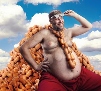 Smiling man sitting on the heap of sausages and with sausages round his neck