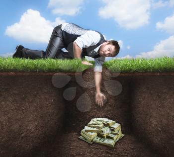 Businessman on knees tries to get treasure in the soil