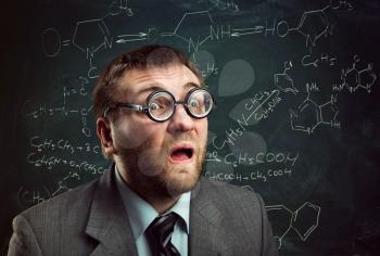 Bizarre professor in glasses thinking over chemical formulas on blackboard
