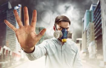 Young man in gas-mask in night town with atmospheric pollution shows stop hand sign
