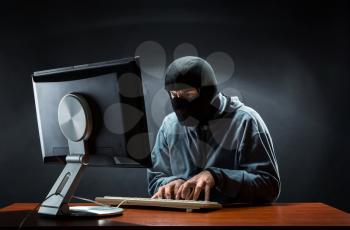 Hacker in balaclava mask stealing information in the office