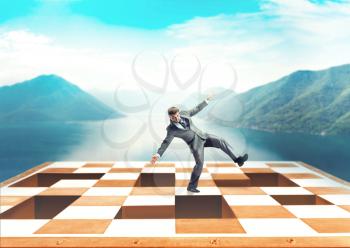 Businessman balancing on the chess board over mountain background