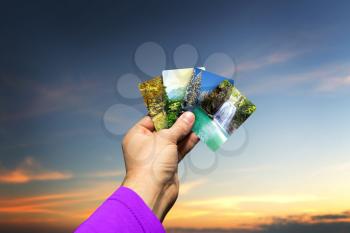 Male hand holding cards with four seasons landscapes over the sky