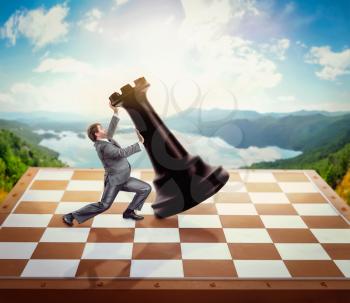 Businessman fighting with a chessman on chess board over nature background
