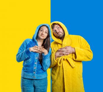 Woman in blue pijamas and man in yellow bathrobe on the blue-and-yellow background