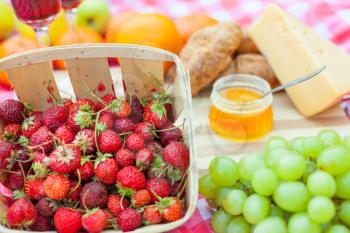 Close up of different products on the blanket prepared for picnic: fruits, croissants, berries and cheese