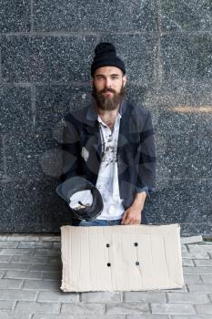 Begar with piece of cardboard and a hat on the street