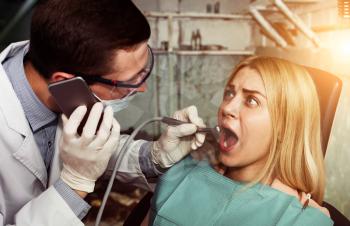 Young dentist working with woman and speaking on the phone in a dirty room, woman is scared