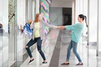 Two women in the shopping mall, one is a shopaholic, another is preventing her friend from buying