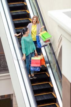 Women talks on the moving staircase holding bags after shopping