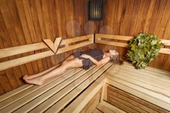 Beauty female in a towel relax on a wooden bench in a sauna.