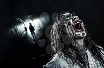 The shouting horror zombie girl in a dark corridor. Halloween.