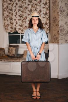 Young female standing in the room with suitcase. Vintage travel waiting concept.