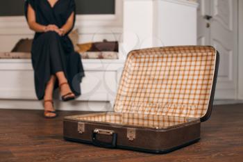 Young woman in black dress sitting on sofa in front of an open suitcase . Retro style.