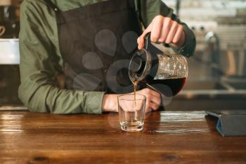 Young male barman pours coffee in a glass. Coffee house on the background.