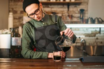 Young male barman pours coffee in a glass. Coffee house on the background.