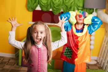 Little girl plays with upset clown at a birthday party. Colorful couch on the background.