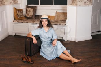 Young girl in light blue dress and white hat sitting on the floor with a suitcase, vintage style. 
