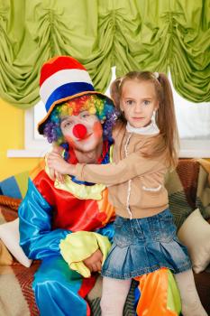 Little girl hugging a cheerful clown with rainbow coloured hair. 