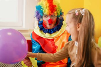 Amusing clown give air balloon to the little girl. Clown in colorful costume on birthday party.