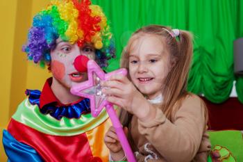 Little girl playing with cheerful clown in funny costume. Friendship concept