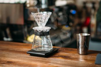 Coffee pot and metal glass on a bar counter. Blury coffee house on background.