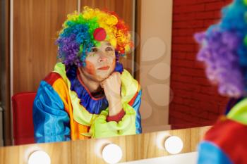 Circus clown looks in a mirror in a make-up room. In waiting of the entertainment.