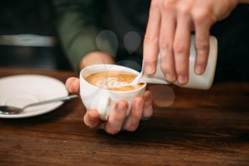 Closeup of male hands adding cream to coffee. Blur table, plate and spoon on the background.