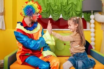 Happy little girl and  clown play palms. Decorate studio on the background.