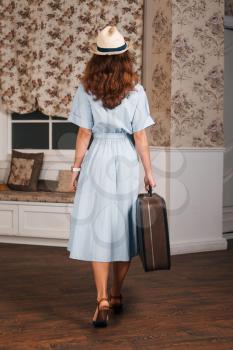 Young female standing in the room with suitcase, view from the back. Vintage travel waiting concept. Retro style.