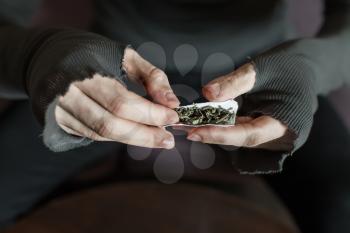 Addict hands making marijuana jamb closeup, wooden background