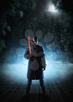 Evil embodiment in hockey mask and black leather coat with bloody baseball bat with a chain wrapped around against dark sky on background.