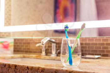 Toothbrushes in a glass on counter. Bathroom with lighted mirror on background