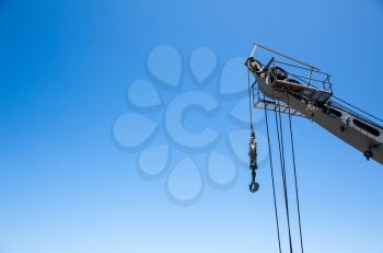 Crane with risen boom on blue sky background. Crane pillar with hook, steel ropes and cables