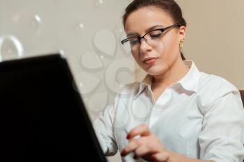 Young female bookkeeper in glasses using laptop in office