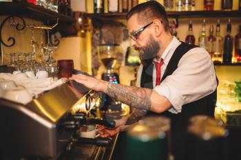 Handsome barista preparing cup of coffee in espresso machine behind bar counter